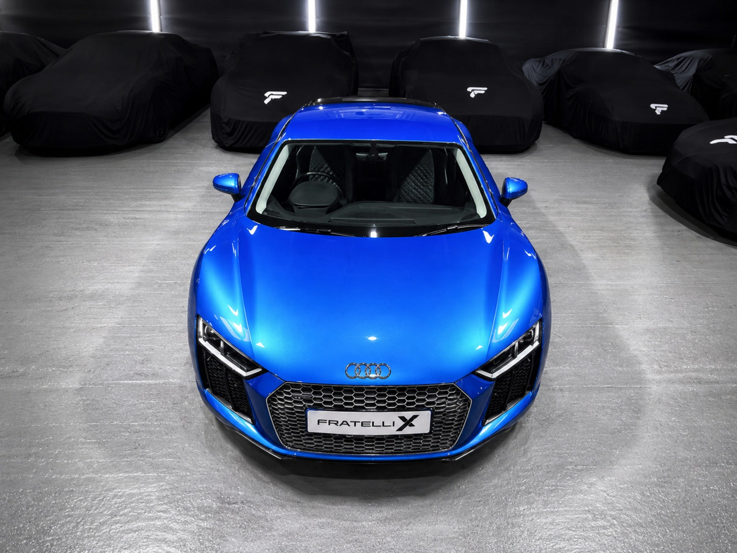 Blue Audi R8 car in a showroom with other cars covered in black car covers.