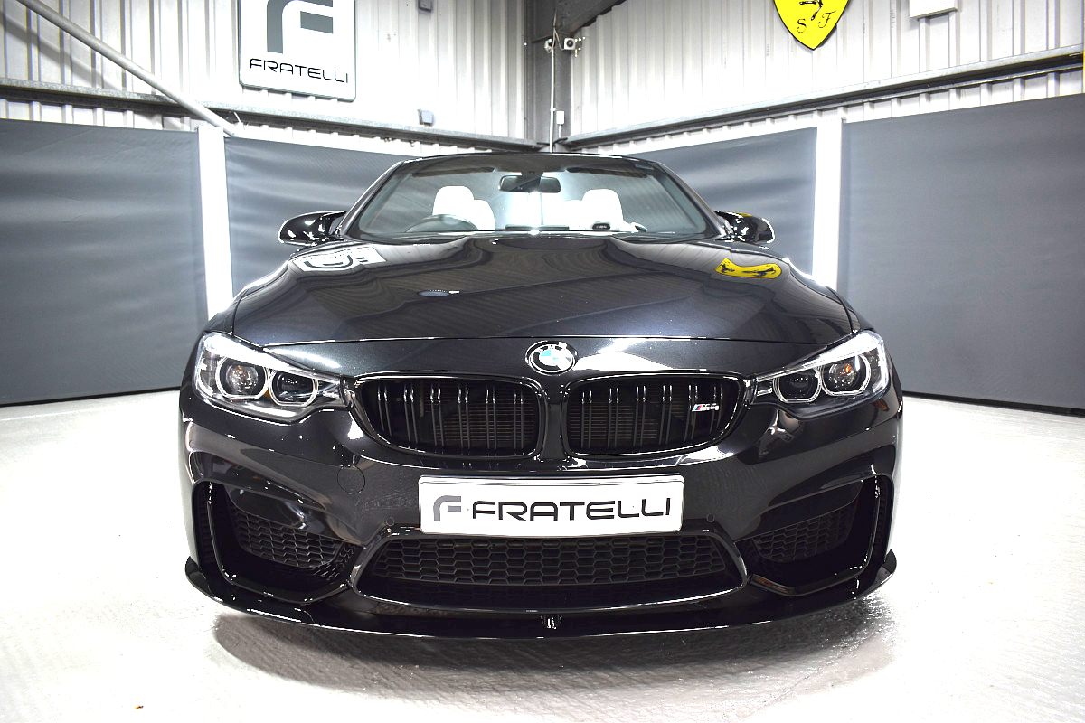 Front of a black BMW M4 convertible with a front splitter and bumper intakes