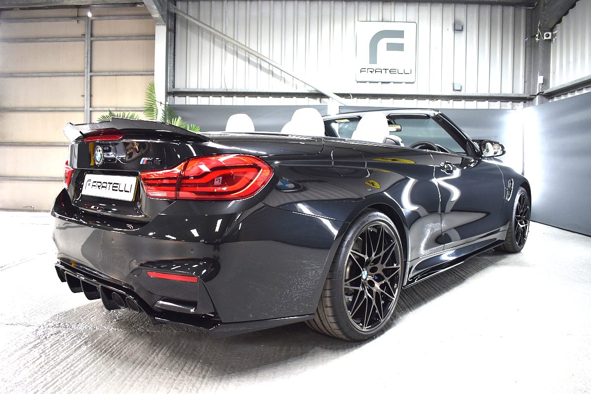 Rear three-quarter of a black BMW M4 convertible with a diffuser and boot spoiler