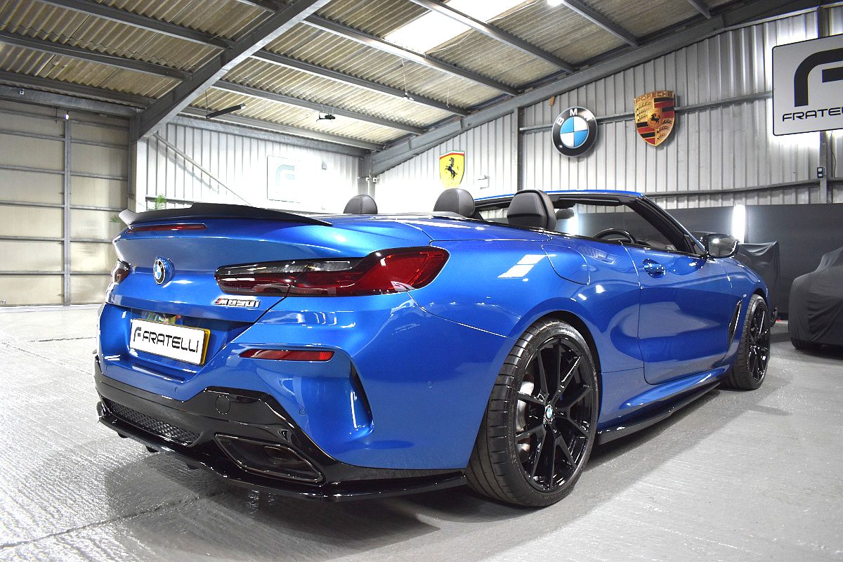 Rear three-quarter of a blue BMW 850i convertible with a side skirt, diffuser and boot spoiler