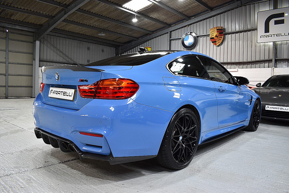 Rear three-quarter of a light blue BMW M4 with a carbon spoiler, side skirt and diffuser