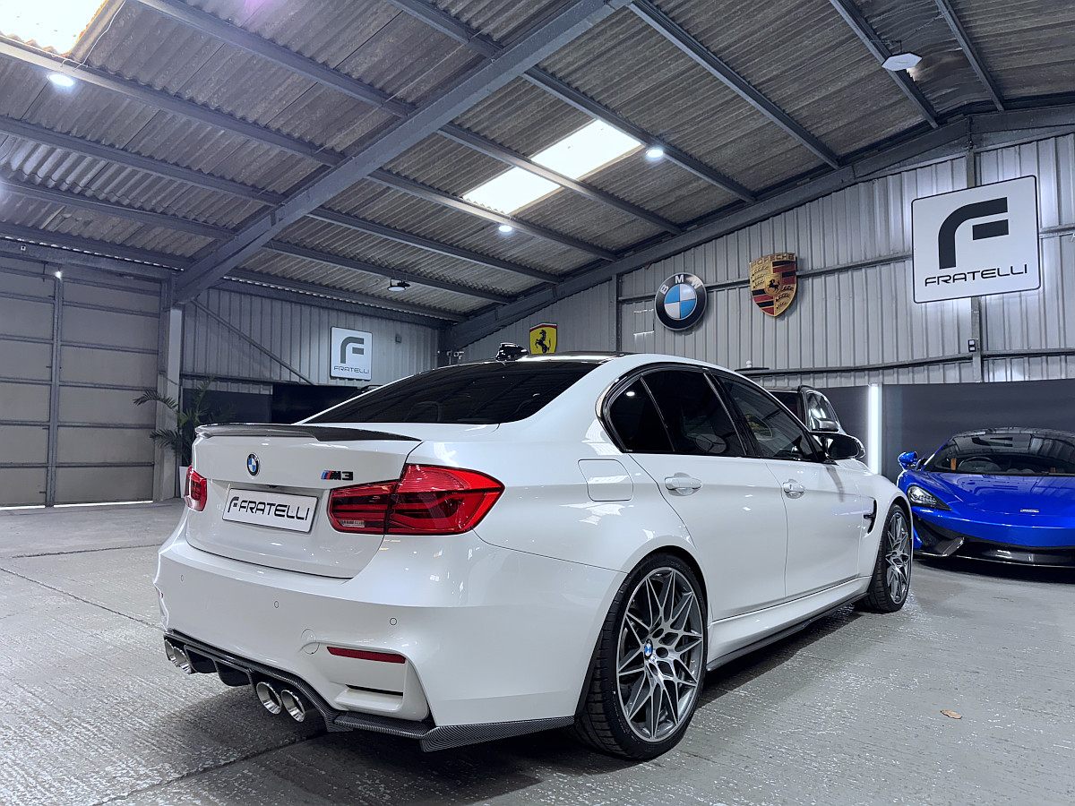 Rear three-quarter of a white BMW M3 saloon with a carbon spoiler and diffuser