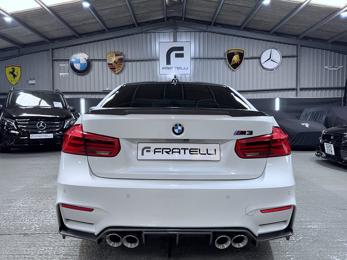Rear of a white BMW M3 saloon with a carbon spoiler, diffuser and quad exhausts